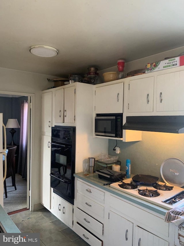 kitchen featuring a warming drawer, under cabinet range hood, white cabinetry, black oven, and white cooktop