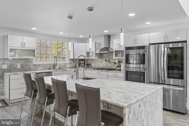 kitchen with a sink, stainless steel appliances, wall chimney exhaust hood, and white cabinetry