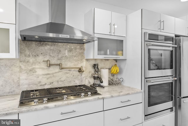 kitchen featuring tasteful backsplash, glass insert cabinets, appliances with stainless steel finishes, white cabinetry, and wall chimney exhaust hood