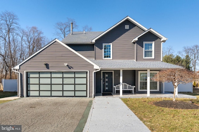 traditional home with a porch, driveway, a shingled roof, and a garage