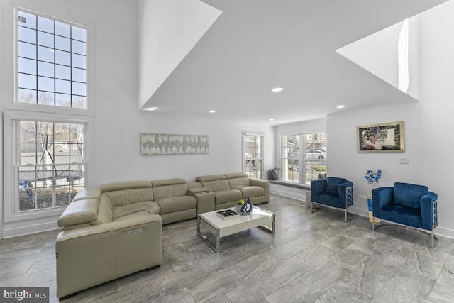 living room featuring plenty of natural light, recessed lighting, baseboards, and a towering ceiling