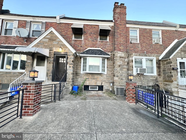 multi unit property featuring cooling unit, central AC unit, a chimney, stone siding, and brick siding