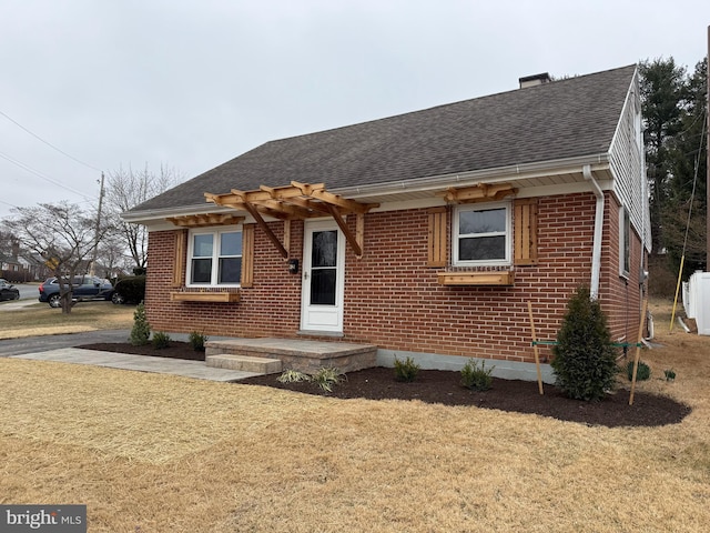 view of front of home with brick siding, a shingled roof, and a front lawn