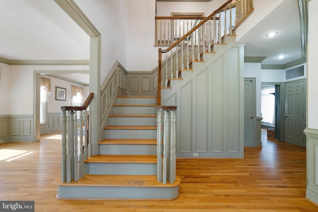 staircase with recessed lighting, a decorative wall, ornamental molding, and wood finished floors