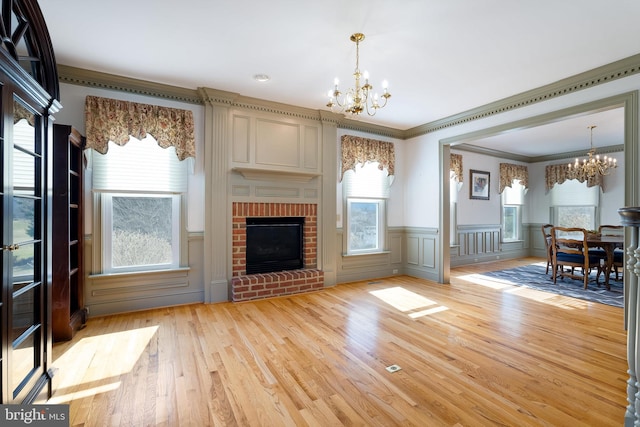 unfurnished living room featuring a fireplace, a notable chandelier, light wood-style floors, and a wealth of natural light