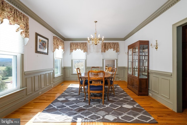 dining area featuring a chandelier, a wainscoted wall, light wood-style flooring, and ornamental molding