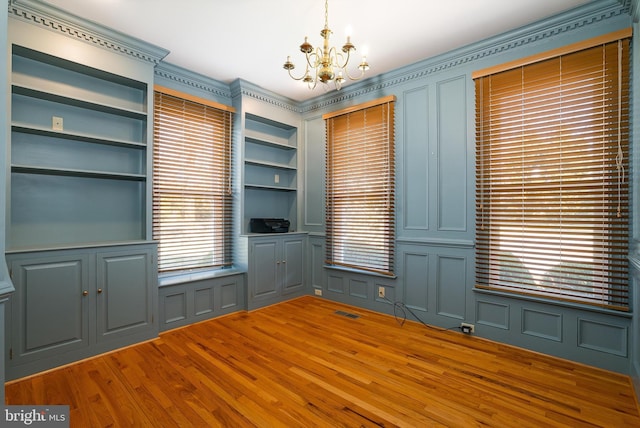 unfurnished dining area featuring an inviting chandelier, a decorative wall, wood finished floors, and visible vents