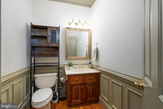 half bathroom featuring a decorative wall, toilet, vanity, and a wainscoted wall