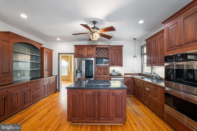 kitchen featuring a sink, dark countertops, a center island, light wood-style floors, and appliances with stainless steel finishes