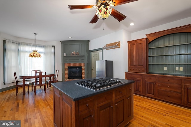 kitchen with dark countertops, a center island, a fireplace, light wood-style floors, and stainless steel appliances