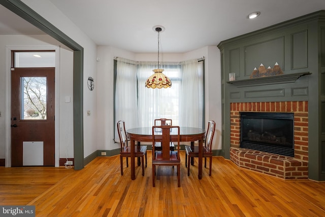 dining area with a brick fireplace, recessed lighting, light wood-style floors, and baseboards