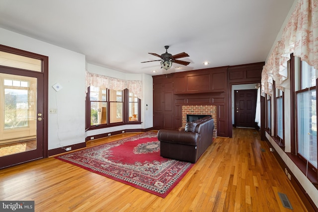 living area with ceiling fan, a fireplace, visible vents, and light wood-type flooring