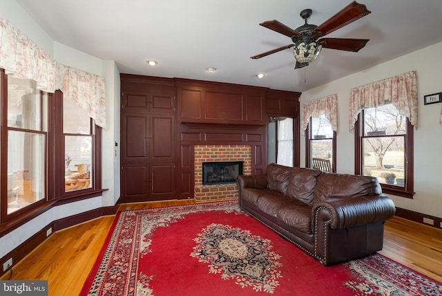 living room featuring baseboards, a ceiling fan, wood finished floors, and a fireplace