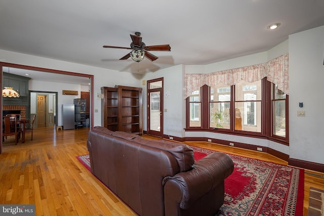 living area with light wood-type flooring, baseboards, a brick fireplace, and a ceiling fan