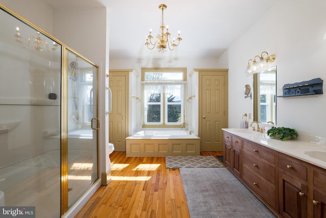 full bath with wood finished floors, double vanity, a sink, a shower stall, and a garden tub