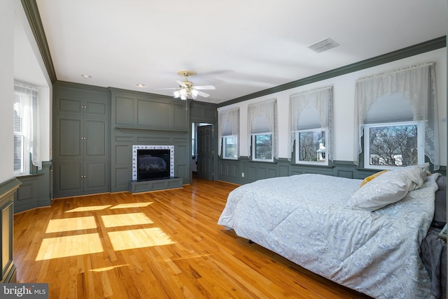 bedroom featuring crown molding, a decorative wall, visible vents, and light wood finished floors