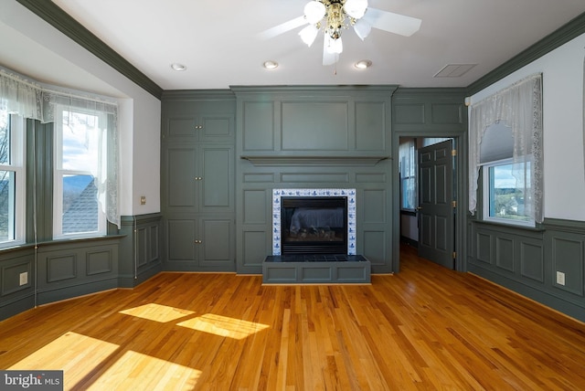 unfurnished living room featuring a glass covered fireplace, a decorative wall, light wood-style floors, and ornamental molding