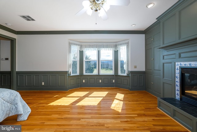 interior space featuring visible vents, crown molding, a tile fireplace, light wood-style floors, and a decorative wall