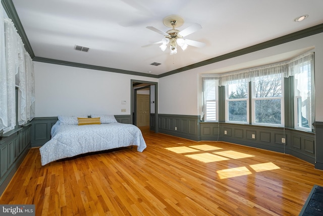 bedroom with light wood-type flooring, visible vents, and a wainscoted wall