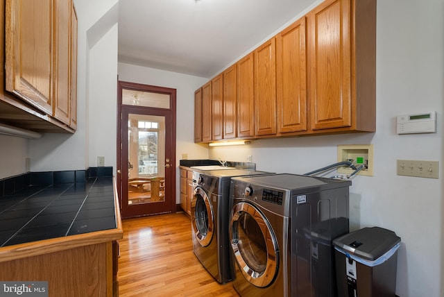 clothes washing area featuring washer and dryer, cabinet space, a sink, and light wood finished floors