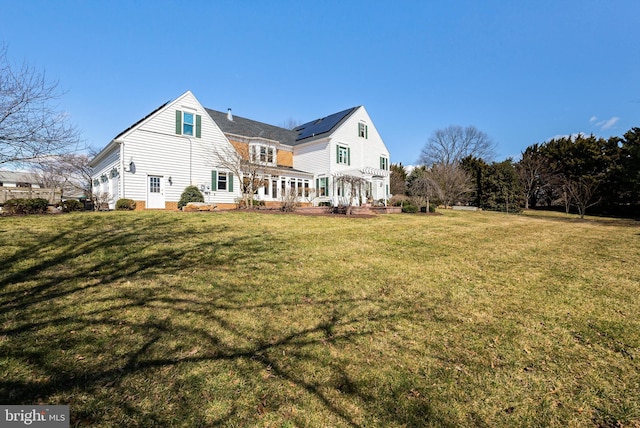 back of property with solar panels, a wooden deck, and a yard