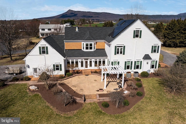 rear view of house with driveway, a lawn, a patio area, a mountain view, and roof mounted solar panels