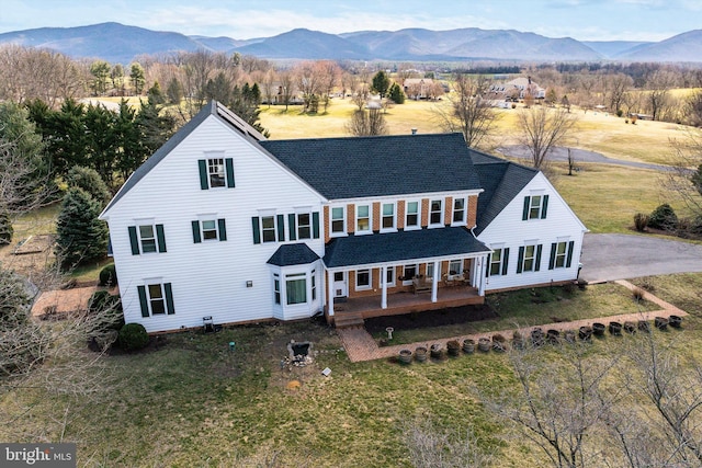 rear view of property with a yard, a mountain view, and roof with shingles