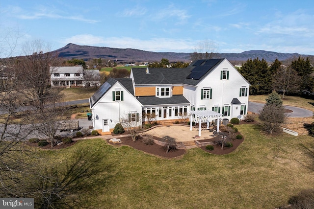 rear view of property with a yard, a pergola, a patio area, a mountain view, and roof mounted solar panels