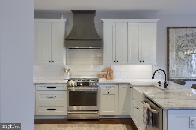 kitchen with light stone countertops, premium range hood, appliances with stainless steel finishes, white cabinetry, and a sink