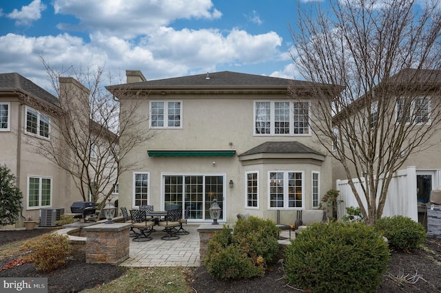 back of house featuring stucco siding, cooling unit, a shingled roof, a chimney, and a patio area