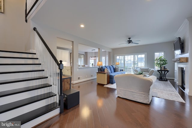 living room featuring a ceiling fan, visible vents, dark wood finished floors, a fireplace, and stairs