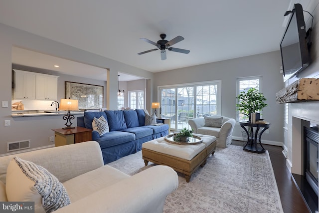 living area with visible vents, baseboards, a glass covered fireplace, a ceiling fan, and dark wood-style flooring