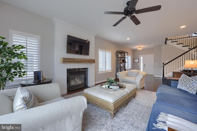 living room with a glass covered fireplace, stairway, wood finished floors, and ceiling fan