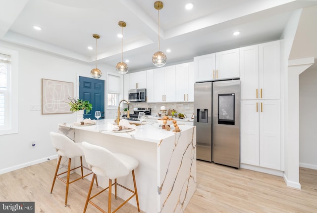 kitchen featuring a tray ceiling, backsplash, appliances with stainless steel finishes, and light wood-style flooring