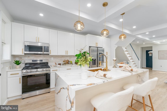 kitchen with a sink, stainless steel appliances, light wood-type flooring, and a tray ceiling