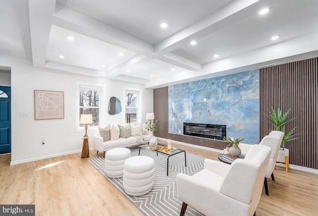 living area featuring beam ceiling, an accent wall, baseboards, and wood finished floors