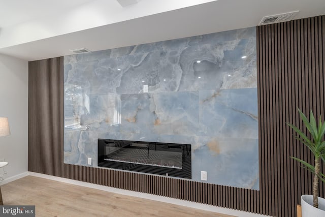 interior details with visible vents, wood finished floors, baseboards, and a glass covered fireplace