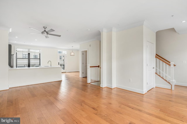 unfurnished living room featuring light wood-type flooring, baseboards, crown molding, and stairway