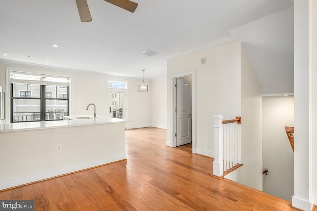 unfurnished living room featuring visible vents, crown molding, baseboards, light wood-type flooring, and a sink