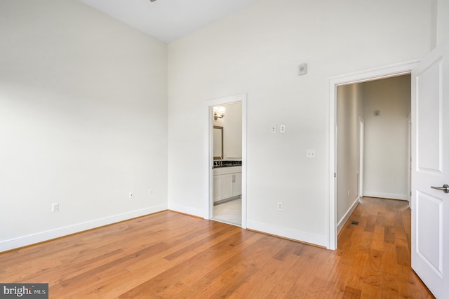 unfurnished bedroom featuring baseboards, light wood finished floors, and connected bathroom