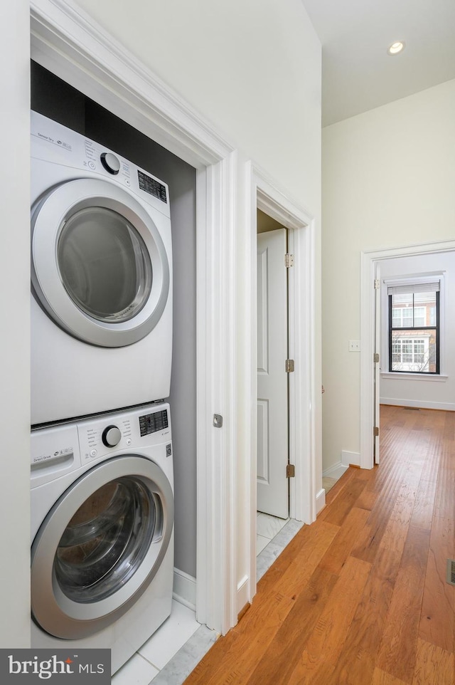 clothes washing area with stacked washer / dryer, recessed lighting, light wood-style floors, and baseboards