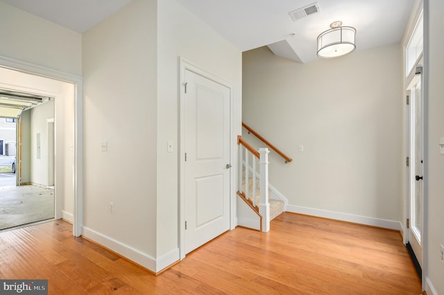 foyer entrance featuring visible vents, baseboards, light wood-style flooring, and stairway