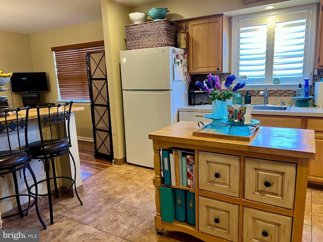 kitchen featuring butcher block countertops, a sink, a kitchen island, freestanding refrigerator, and baseboards