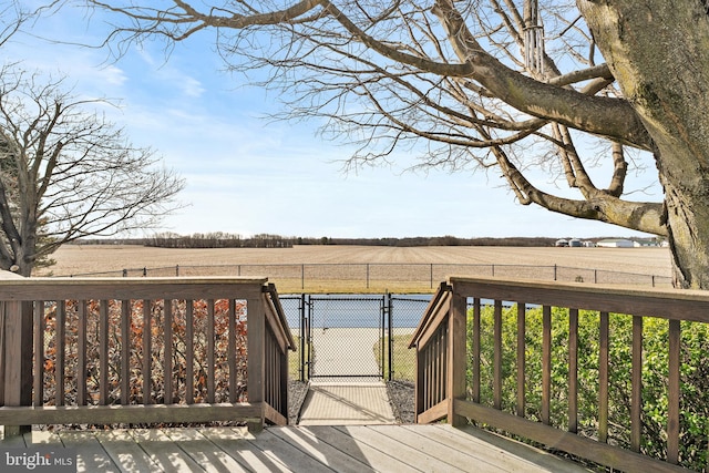 deck featuring a rural view, fence, and a gate