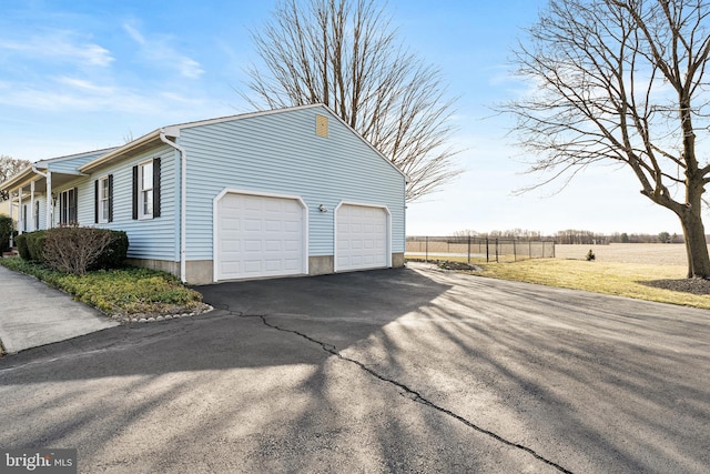 view of side of home featuring aphalt driveway, an attached garage, and fence