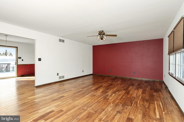 unfurnished room with visible vents, a healthy amount of sunlight, wood finished floors, and ceiling fan with notable chandelier