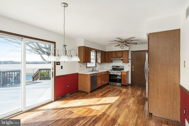 kitchen featuring under cabinet range hood, light countertops, light wood-style flooring, appliances with stainless steel finishes, and a sink