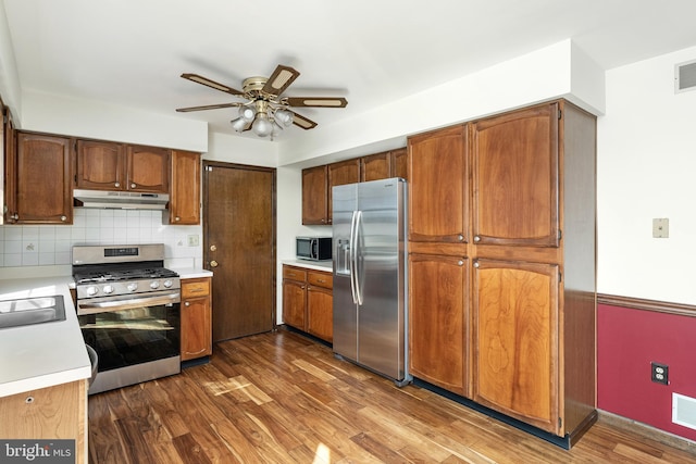 kitchen featuring under cabinet range hood, stainless steel appliances, light countertops, and dark wood-type flooring