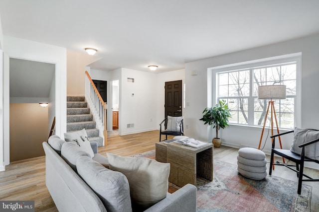 living room featuring stairs, light wood-style flooring, and baseboards