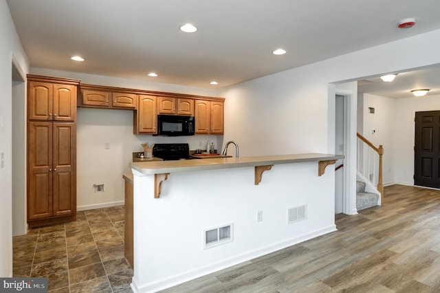 kitchen with recessed lighting, visible vents, black appliances, and a breakfast bar area